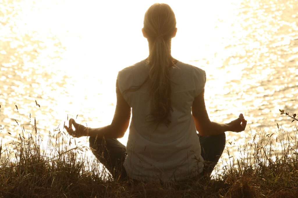 Woman meditating by the water during sunset, sitting in a cross-legged position with hands in mudra — promoting mindfulness, mental clarity, and emotional balance. Reflects the holistic healing philosophy of Anupama Wellness, a UK-based Ayurvedic and wellness practitioner.jpg