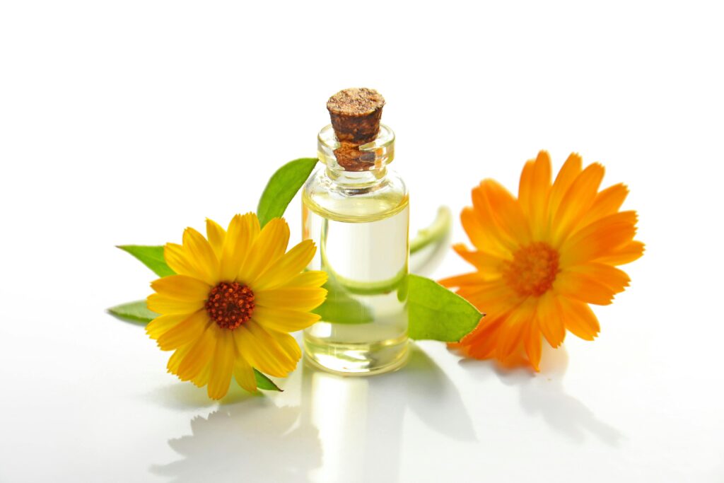 A bottle of calendula oil surrounded by fresh calendula flowers, highlighting its use in skin care used for Aromatherapy at Anupama Wellness-UK.jpg